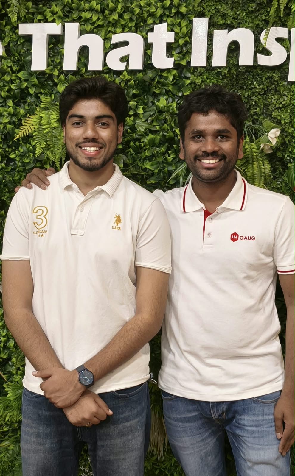 Victor and Hari Pavan smiling in white polos in front of a green plant wall