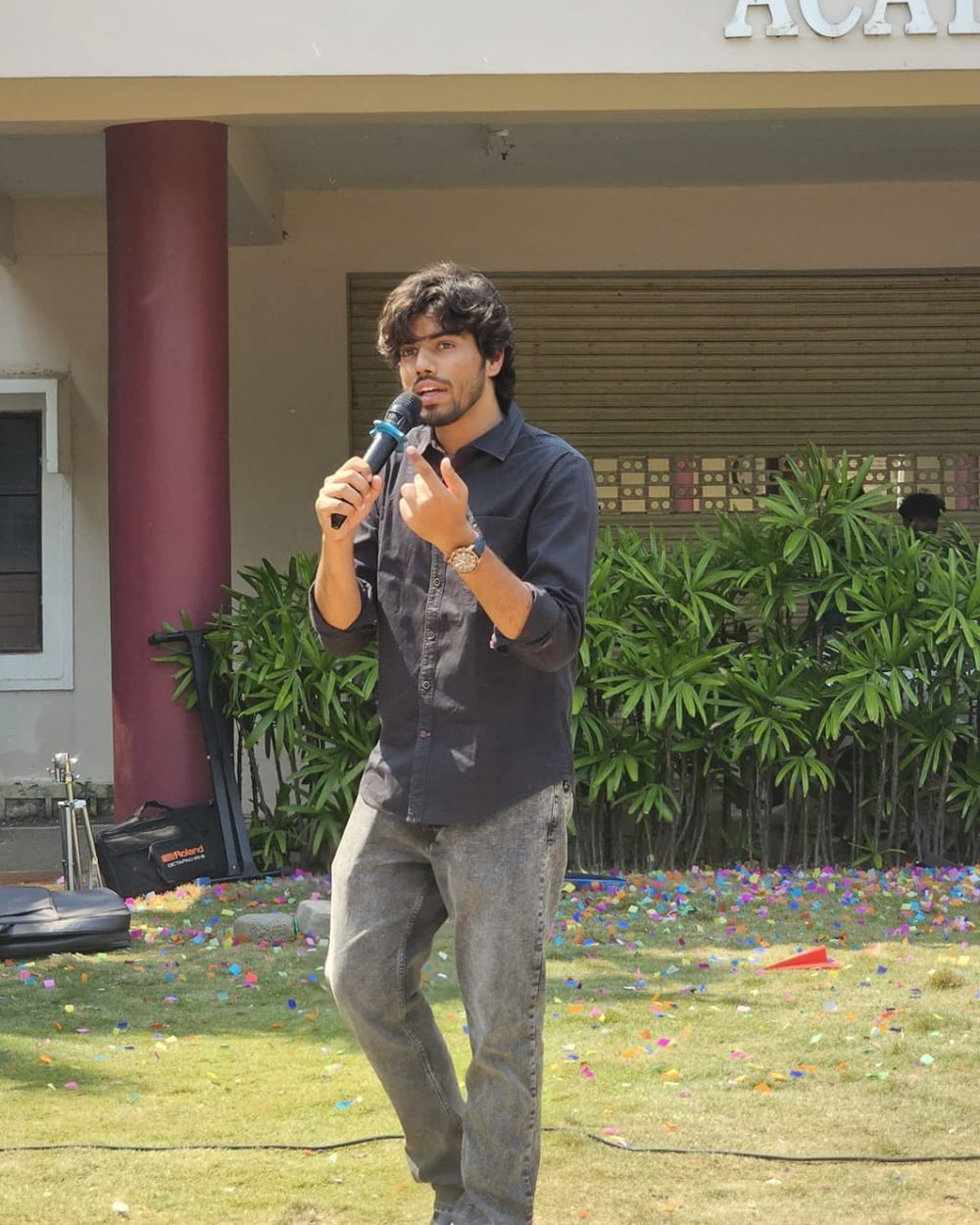Victor speaking into a microphone on the lawn at the TEDxACE banner launch, ACE Engineering College