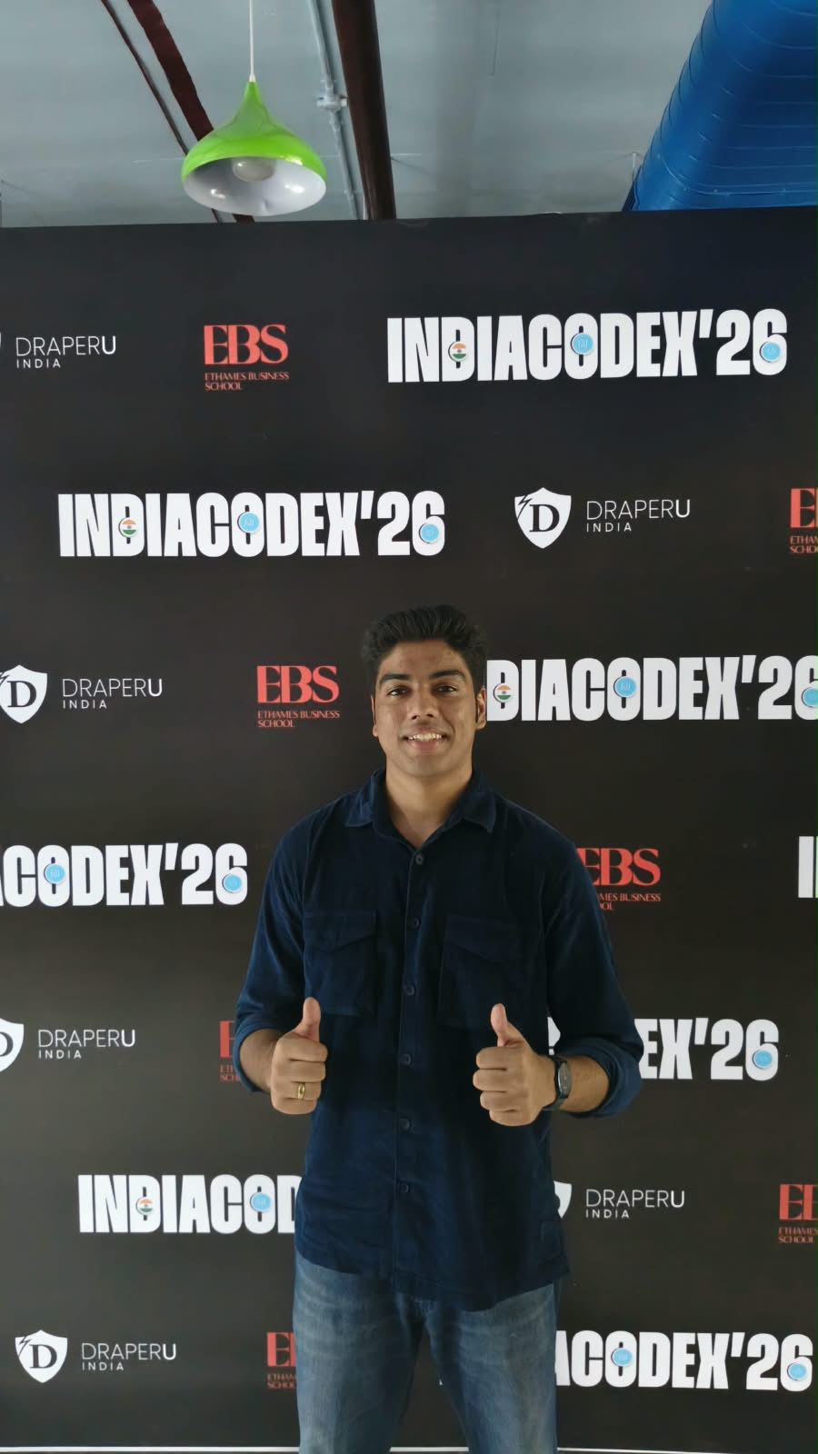 Victor giving two thumbs up in front of the IndiaCodeX'26 backdrop with DraperU India and EBS logos