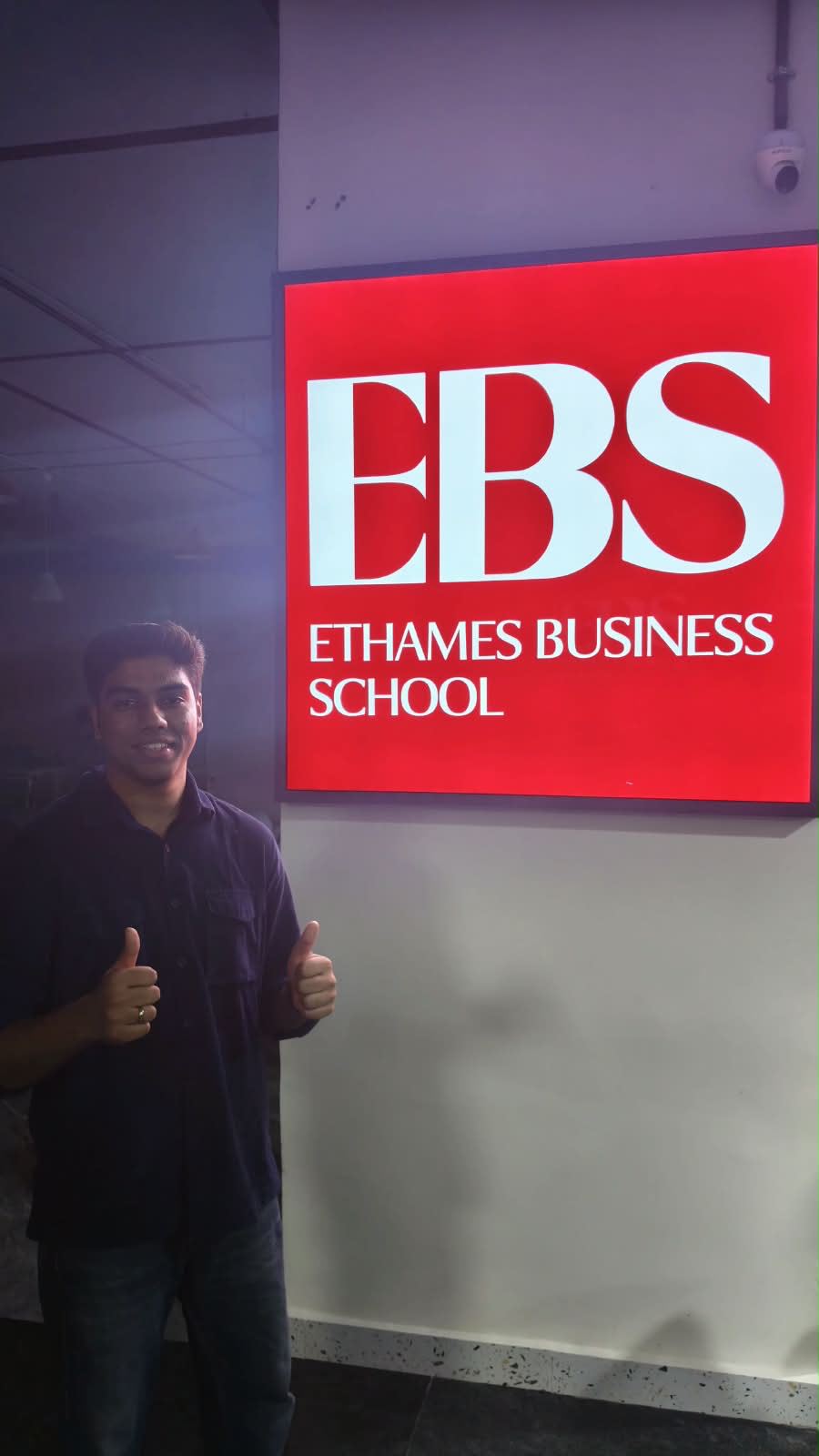 Victor giving a thumbs up beside the red Ethames Business School sign