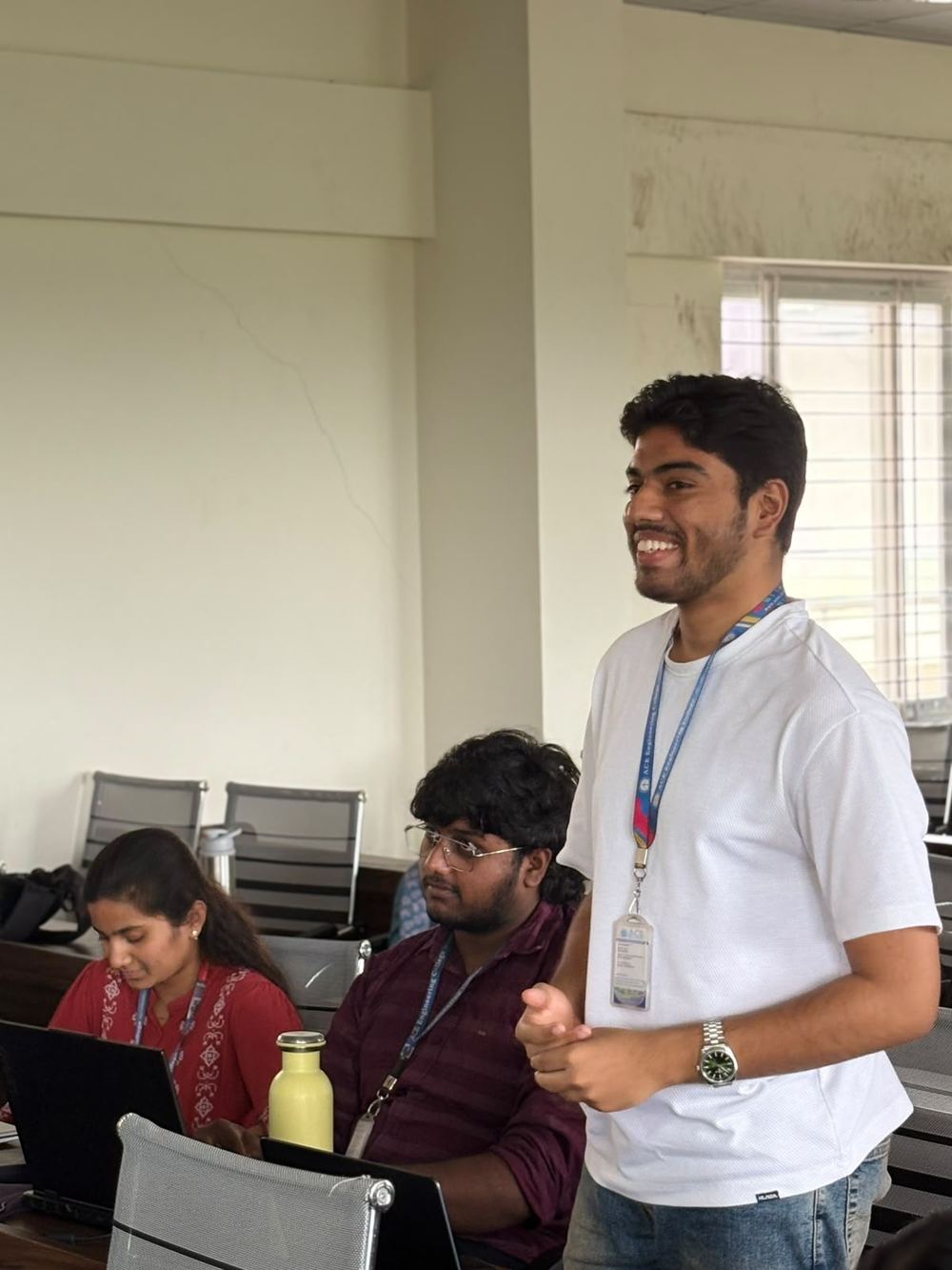 Victor standing and smiling while speaking to classmates seated at laptops