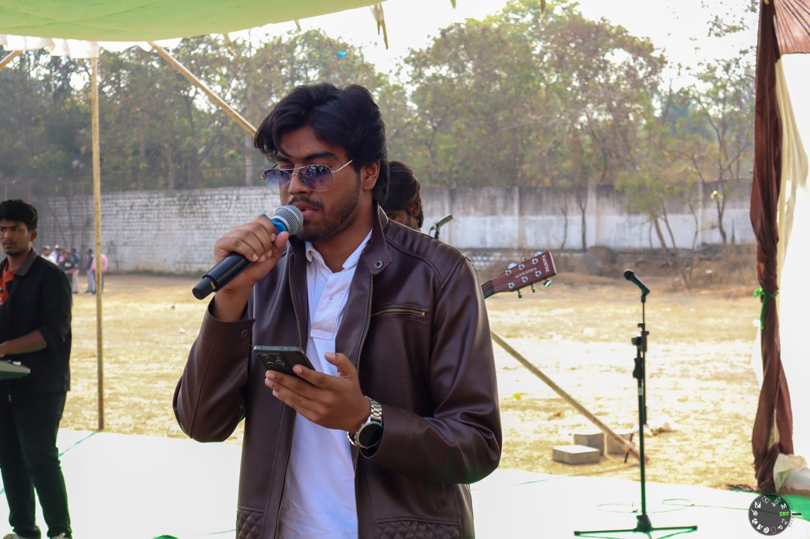 Victor singing with a microphone and reading lyrics from his phone on the CBIT stage