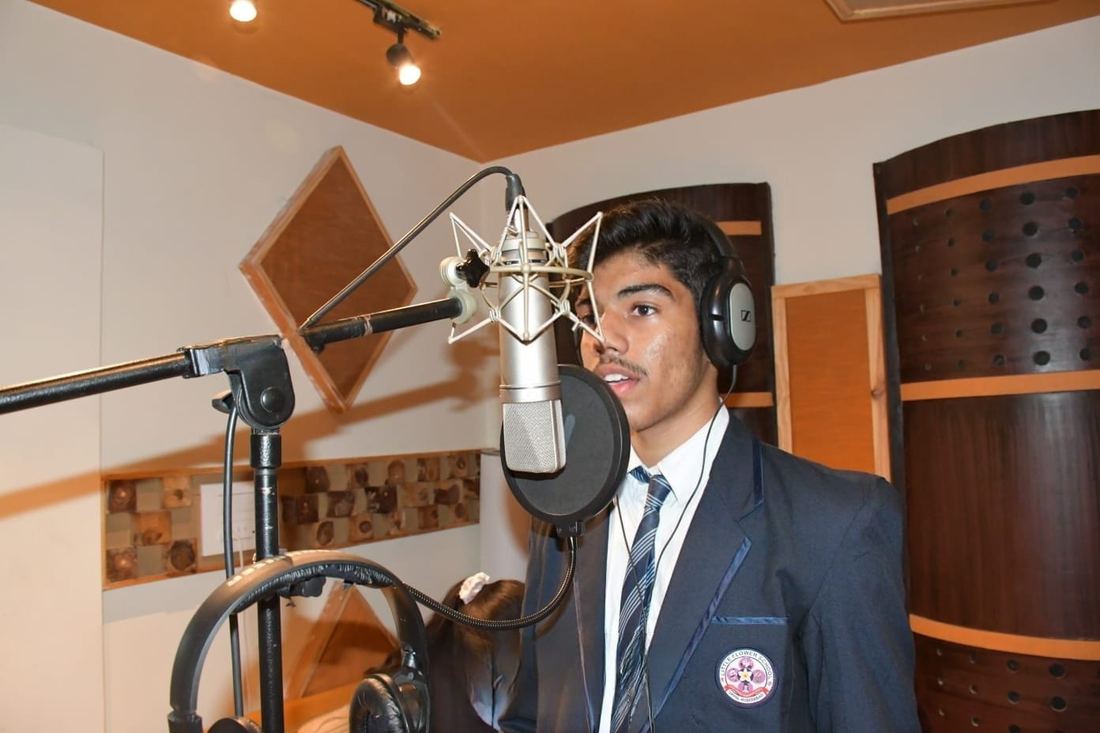 Victor in school uniform singing into a studio condenser microphone with headphones on